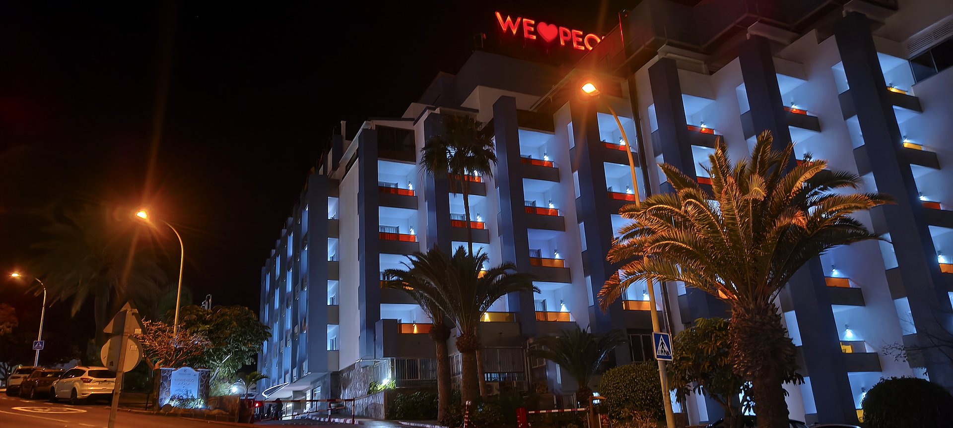 Noční pohled na hotel Paradise Park Fun Lifestyle Hotel v Los Cristianos – osvětlená fasáda s nápisem WE LOVE PEOPLE
